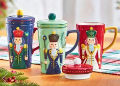 three colorful mugs sitting on top of a table next to a christmas tree in the background