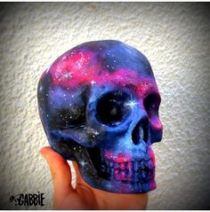 a hand holding up a blue and pink skull with stars on it's face