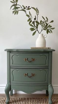 a green dresser sitting on top of a rug next to a white vase