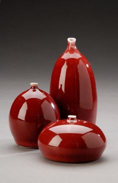 three red vases sitting next to each other on a gray surface with white trim