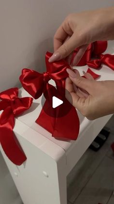 someone is wrapping a red bow on a white box that has been tied with ribbon