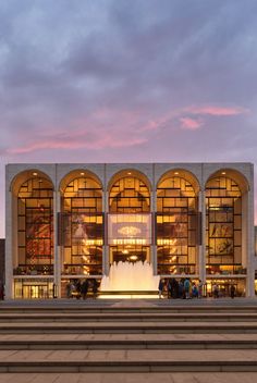 the building is lit up at night and has many windows on each side, along with stairs leading up to it