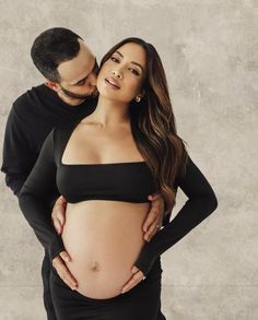 a pregnant woman in a black dress is holding her husband's belly while they pose for the camera