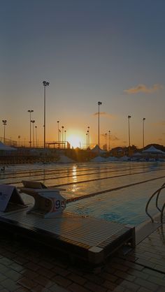 an empty swimming pool with the sun setting in the background and some lights on poles