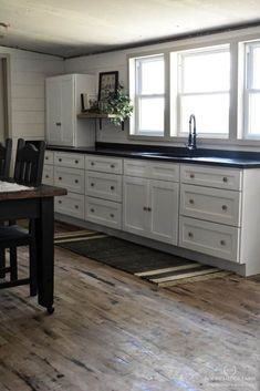 a kitchen with white cabinets and black counter tops is seen in this image, while the light shines through the window onto the hardwood floor