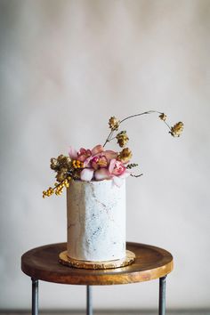 a white cake with pink flowers on top sitting on a wooden table next to a gray wall