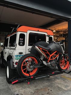 an orange and black motorcycle is parked in front of a white truck with red rims