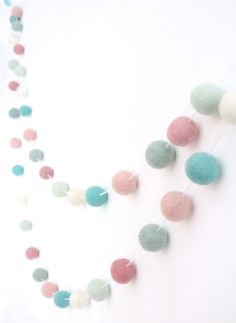 a string of felt balls hanging from the ceiling in front of a white wall with blue, pink and green colors