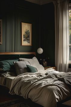 an unmade bed sitting next to a window in a room with dark green walls