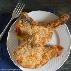 two pieces of fried chicken on a white plate with a fork and knife next to it