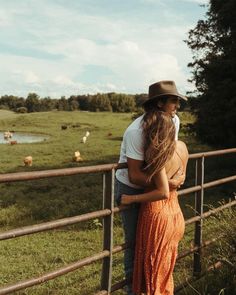 a man and woman standing next to each other near a fence with cows in the background