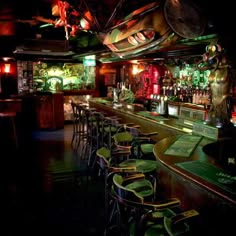 a dimly lit bar with many stools and green lights on the ceiling, in a dark room