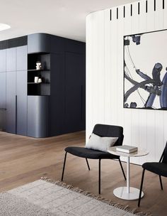 two chairs and a table in a room with white walls, wood flooring and black cabinets