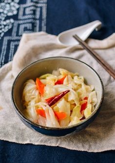 a bowl filled with cabbage and carrots next to chopsticks on a napkin