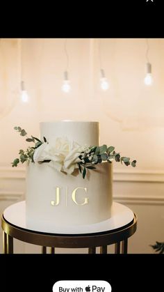 a white wedding cake sitting on top of a gold stand with greenery around it