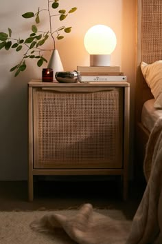 a nightstand with a lamp on top of it next to a bed and a plant