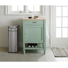 a small green cabinet next to a trash can in a white room with a rug on the floor