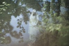 a woman in a white dress is walking through the woods with her veil draped over her head