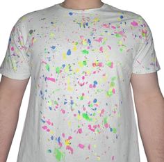 a man wearing a white t - shirt with multicolored paint splatters on it