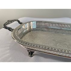 an ornate silver tray with handles on a white tableclothed surface, resting on a pillow