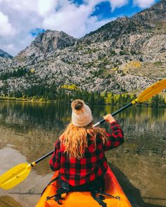 a woman is paddling her kayak on the water in front of some mountains