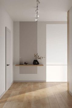 an empty room with wooden flooring and white walls in the center is a plant on a shelf