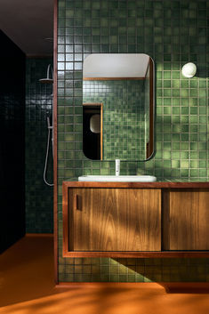 a green tiled bathroom with wooden cabinets and mirror above the sink, along with a shower head