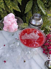 a table topped with two glasses filled with liquid and flowers next to each other on top of a white cloth