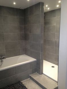 a bathroom with grey tiles and a white bathtub next to a walk in shower