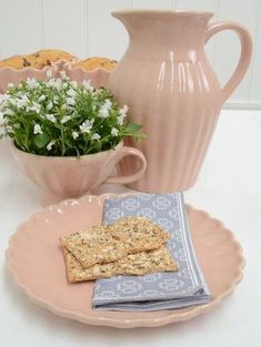 a plate with crackers on it next to a pink vase and flower in the background