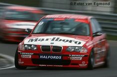 a red and white car driving down a race track next to other cars in motion