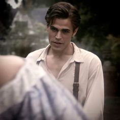 a man with suspenders and a white shirt is looking at another man in the mirror