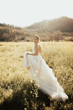 a woman in a wedding dress walking through a field