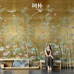 a woman sitting on a bench in front of a wall with flowers and birds painted on it