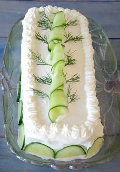 a cake with cucumber slices on it sitting on a glass platter, ready to be eaten