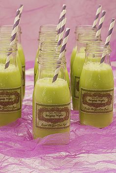 six glasses filled with green smoothie and drinking straws on top of a pink table cloth