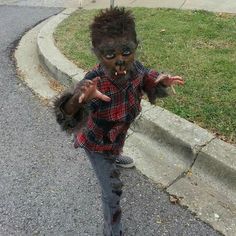 a young boy dressed up as a zombie walking down the street with his hands in the air