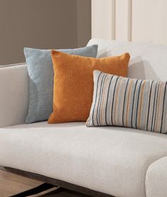 a white couch with three different colored pillows on it's back and one orange pillow sitting on top of the sofa