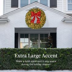 a large wreath on the front of a white house with a red bow hanging from it's door