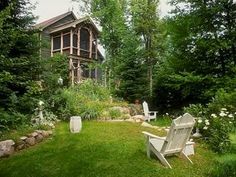 two white chairs sitting on top of a green grass covered field next to a house