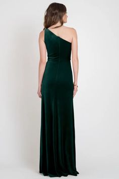 a woman in a long green dress with one shoulder and open back, looking down at the