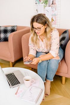 a woman sitting on a pink couch looking at her cell phone and holding a camera