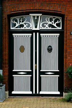 two black and white double doors in front of a red brick building with potted plants