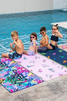 four children sitting on the ground in front of a swimming pool with towels around them