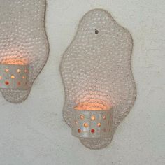 two wall sconces with lit candles attached to them on a white wall background