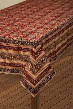 a table covered with a red, blue and white paisley print cloth sitting on top of a wooden floor