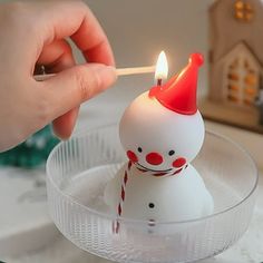 a person lighting a candle with a small snowman figure on top of the candle holder