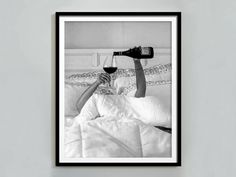 a black and white photo of a person laying in bed with a glass of wine