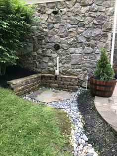 an outdoor shower in the corner of a stone walled building with plants and rocks around it