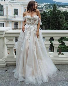 a woman standing on top of a balcony wearing a wedding dress with an off the shoulder design